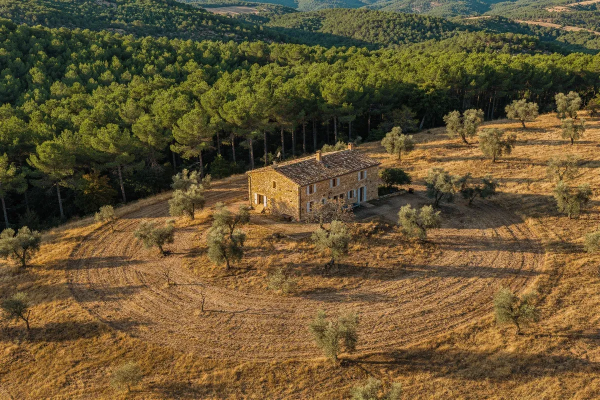 Vue aérienne d'une maison en pierre avec zone débroussaillée de 50 m autour, contrastant avec la forêt environnante