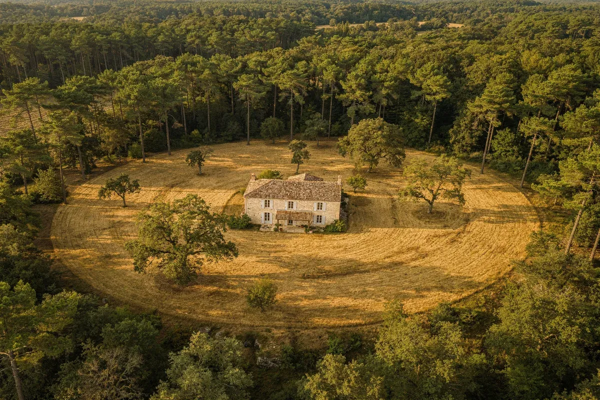 Vue aérienne d'une maison isolée en forêt avec zone de débroussaillement circulaire autour